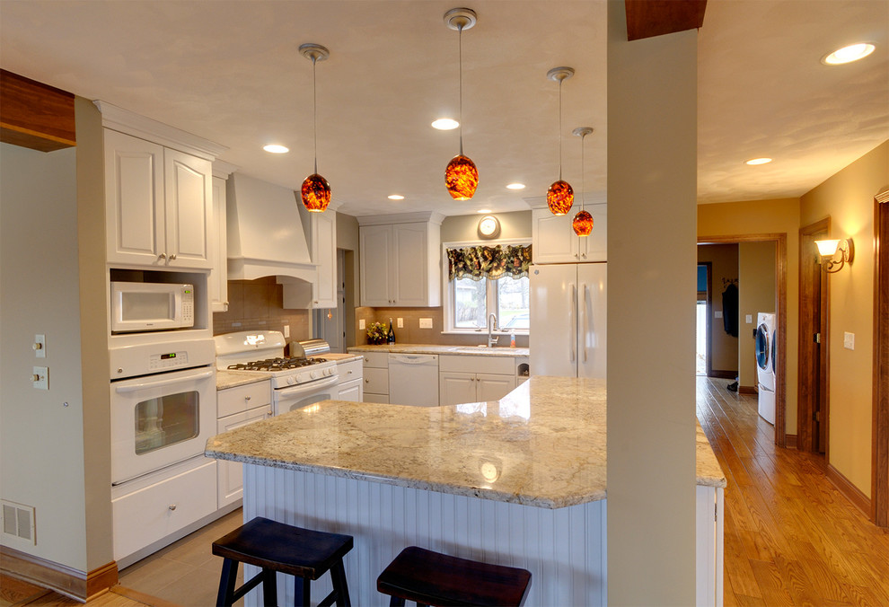 Example of a mid-sized transitional u-shaped medium tone wood floor eat-in kitchen design in Chicago with a drop-in sink, raised-panel cabinets, white cabinets, wood countertops, beige backsplash, stone slab backsplash, white appliances and no island