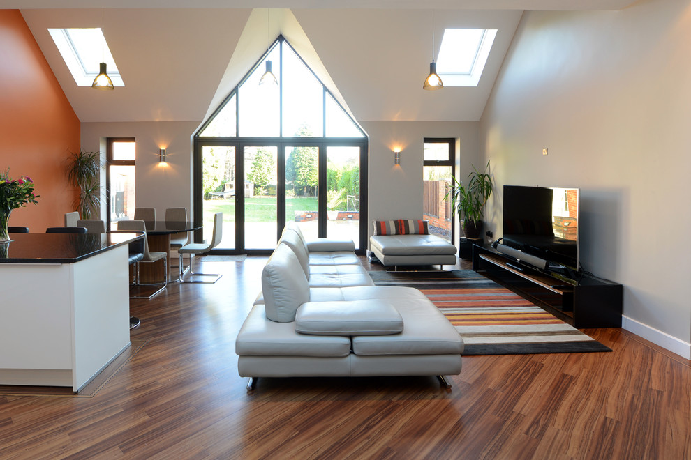 Contemporary open concept living room in West Midlands with orange walls and a freestanding tv.