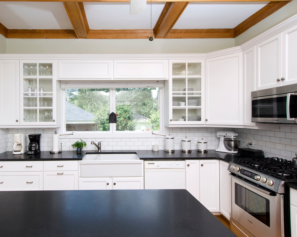 Mid-sized transitional u-shaped medium tone wood floor and brown floor enclosed kitchen photo with a farmhouse sink, shaker cabinets, white cabinets, granite countertops, white backsplash, ceramic backsplash, stainless steel appliances and an island