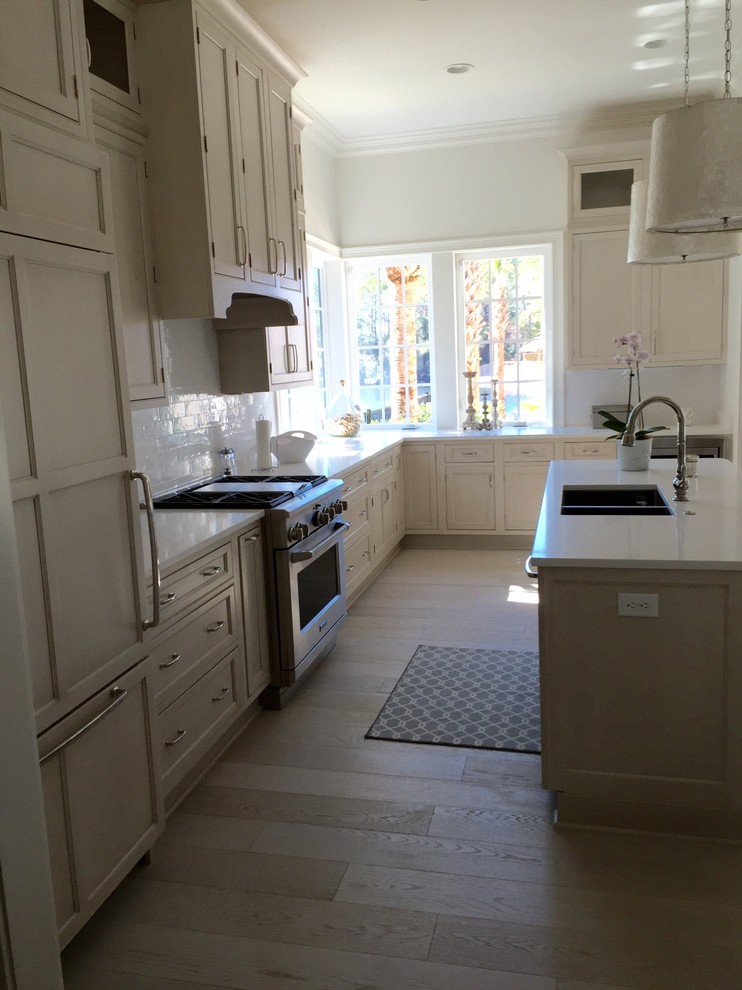 This is an example of a large transitional l-shaped eat-in kitchen in Miami with an undermount sink, beaded inset cabinets, white cabinets, white splashback, stainless steel appliances and with island.