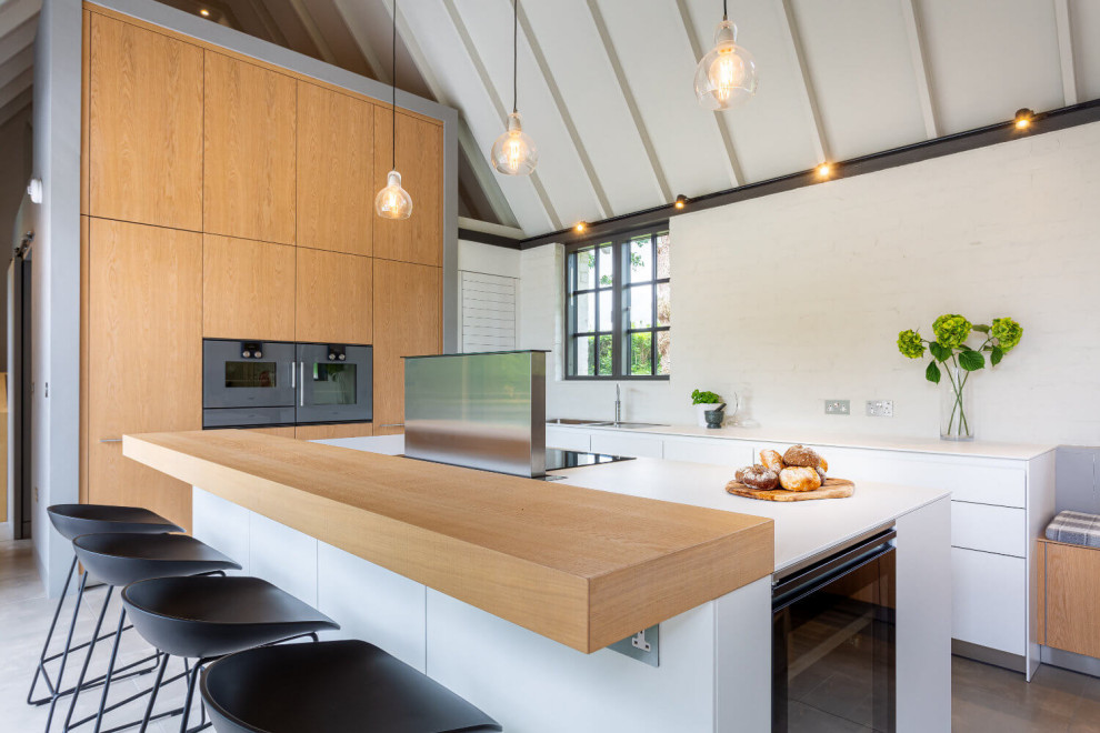 Photo of an expansive contemporary l-shaped open plan kitchen in Cardiff with an integrated sink, flat-panel cabinets, light wood cabinets, laminate benchtops, white splashback, glass sheet splashback, coloured appliances, porcelain floors, with island, white benchtop and vaulted.