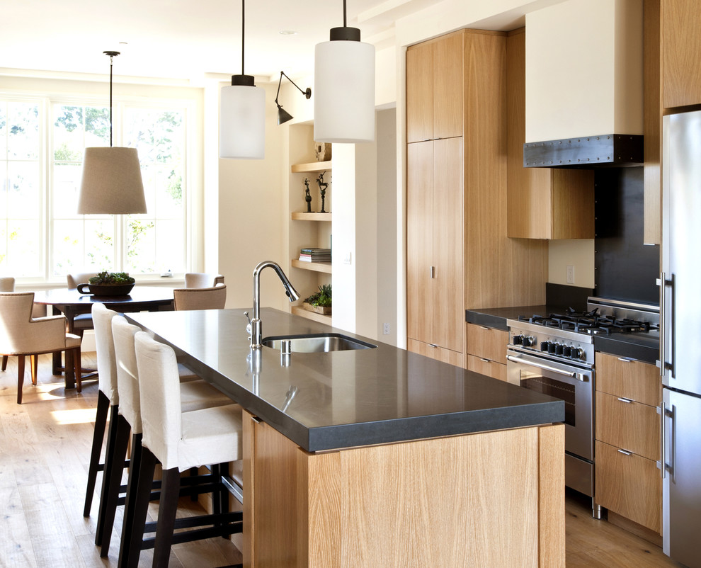 This is an example of a contemporary galley eat-in kitchen in San Francisco with stainless steel appliances, a single-bowl sink, flat-panel cabinets and light wood cabinets.