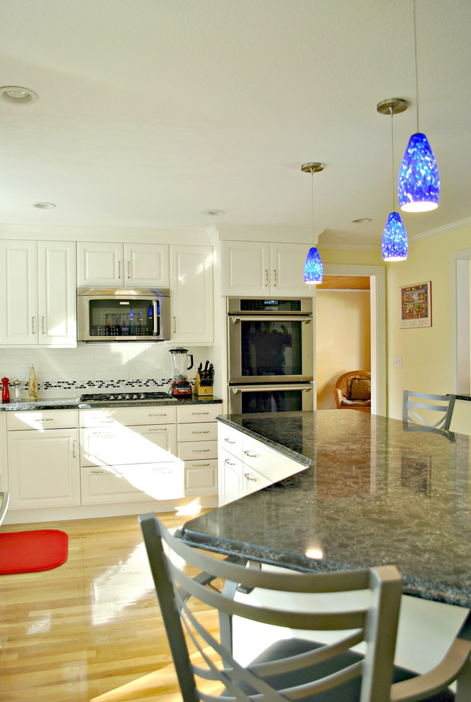 Photo of a mid-sized traditional l-shaped eat-in kitchen in Boston with an undermount sink, raised-panel cabinets, white cabinets, quartz benchtops, white splashback, ceramic splashback, stainless steel appliances, medium hardwood floors and with island.