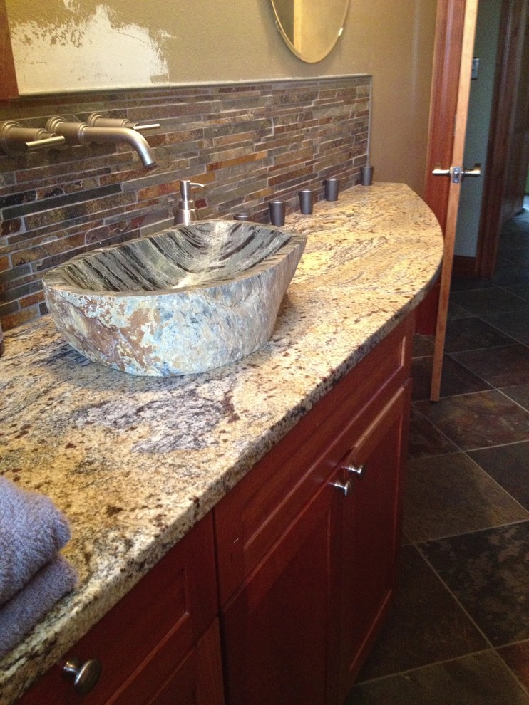Transitional multicolored tile and stone tile doorless shower photo with a vessel sink, shaker cabinets, medium tone wood cabinets, granite countertops and a two-piece toilet