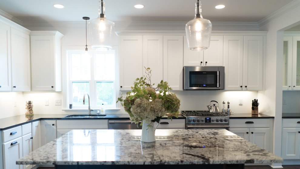 Example of a mid-sized transitional l-shaped dark wood floor open concept kitchen design with an undermount sink, shaker cabinets, white cabinets, granite countertops, gray backsplash, stainless steel appliances and an island