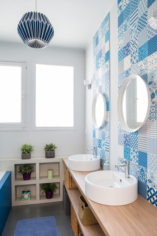 Photo of a mediterranean bathroom in Toulouse with open cabinets, blue tile, white tile, cement tile, white walls, concrete floors, a vessel sink, wood benchtops, grey floor and beige benchtops.