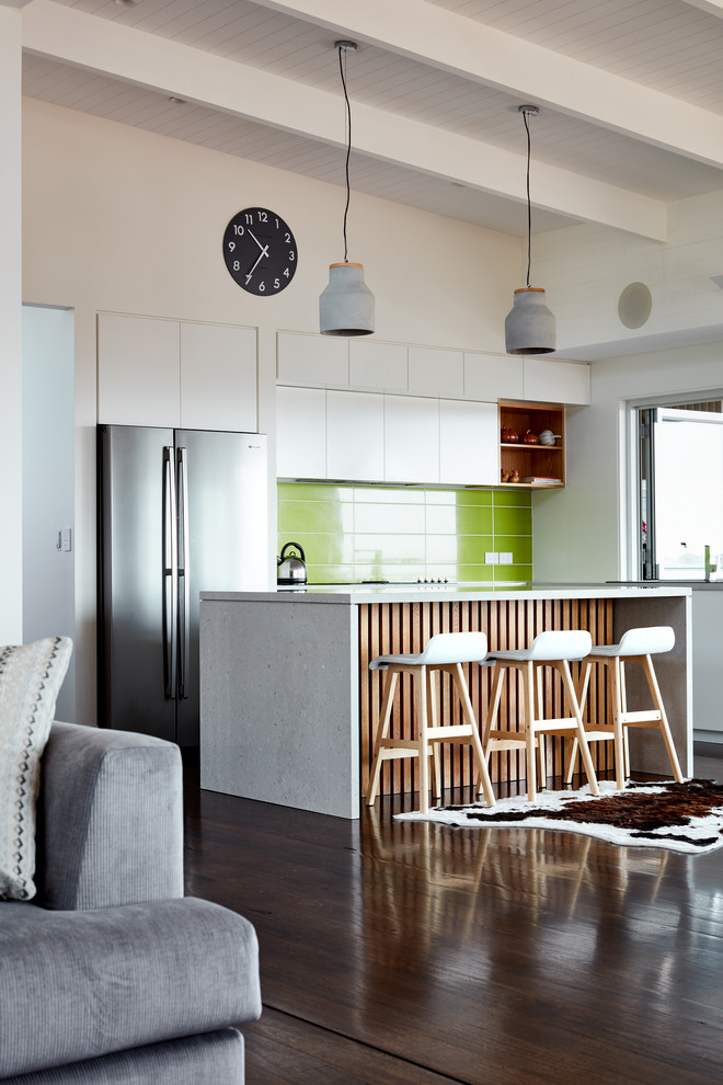 This is an example of a contemporary galley kitchen in Sydney with flat-panel cabinets, white cabinets, green splashback, stainless steel appliances, dark hardwood floors and with island.