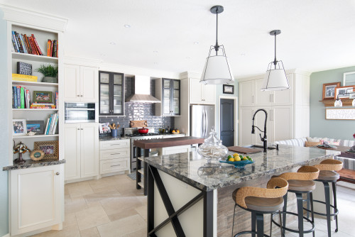 Airy open-plan kitchen with cream shaker RTA cabinets, glass-front uppers around a stainless hood, a granite island with black X-base, pendant lights, and built-in bookshelves.