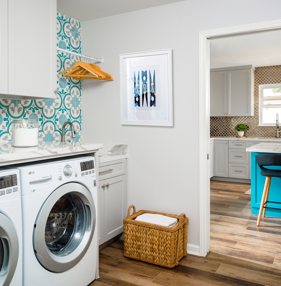 This is an example of a small transitional single-wall dedicated laundry room in Houston with an undermount sink, shaker cabinets, grey cabinets, solid surface benchtops, grey walls, porcelain floors, a side-by-side washer and dryer, white benchtop and brown floor.