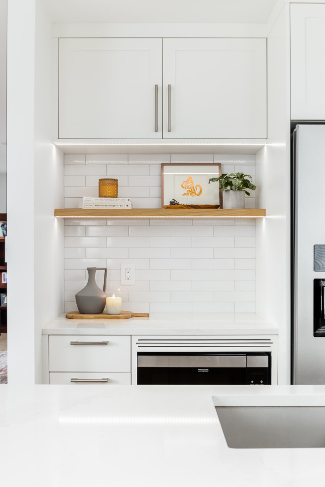 Example of a mid-sized transitional l-shaped light wood floor and beige floor eat-in kitchen design in Vancouver with an undermount sink, shaker cabinets, white cabinets, quartzite countertops, white backsplash, subway tile backsplash, stainless steel appliances, an island and white countertops