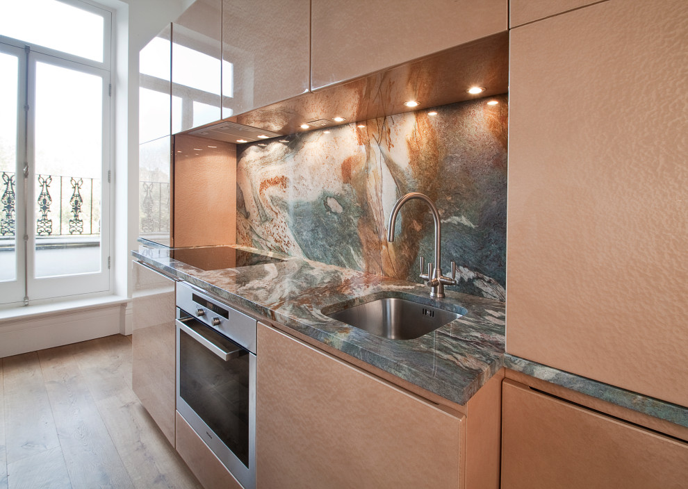 Large contemporary galley kitchen in London with a triple-bowl sink, flat-panel cabinets, multi-coloured splashback, stainless steel appliances, light hardwood floors, beige floor and multi-coloured benchtop.