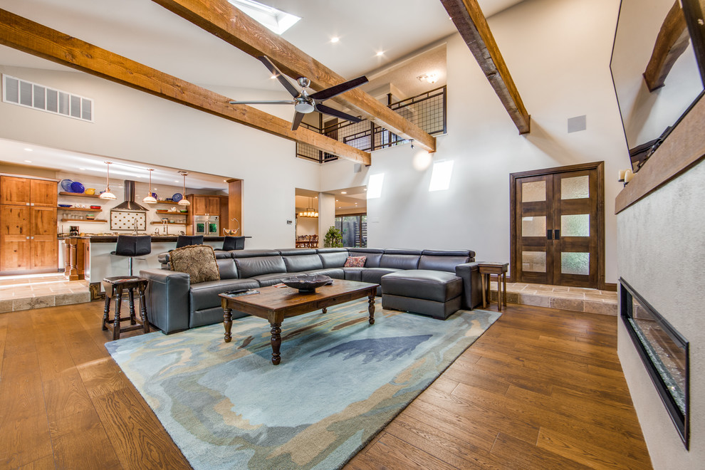 This is an example of a large transitional open concept living room in Austin with white walls, light hardwood floors, a ribbon fireplace, a plaster fireplace surround, a wall-mounted tv and brown floor.