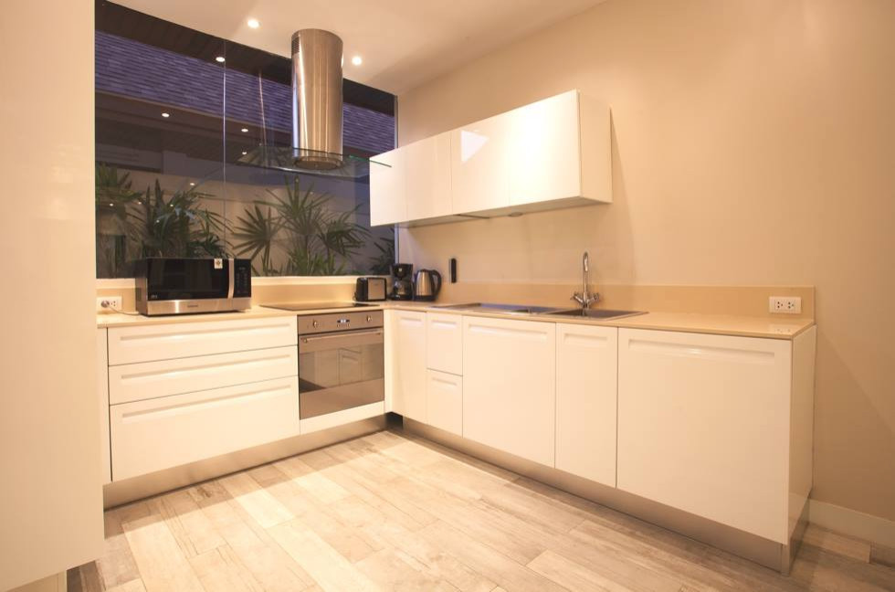 Photo of a mid-sized tropical l-shaped eat-in kitchen with a single-bowl sink, flat-panel cabinets, white cabinets, marble benchtops, black appliances and grey floor.