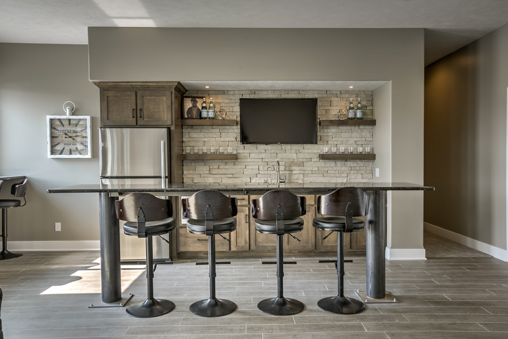 Inspiration for a large traditional single-wall seated home bar in Omaha with an undermount sink, shaker cabinets, dark wood cabinets, beige splashback, stone tile splashback and grey floor.