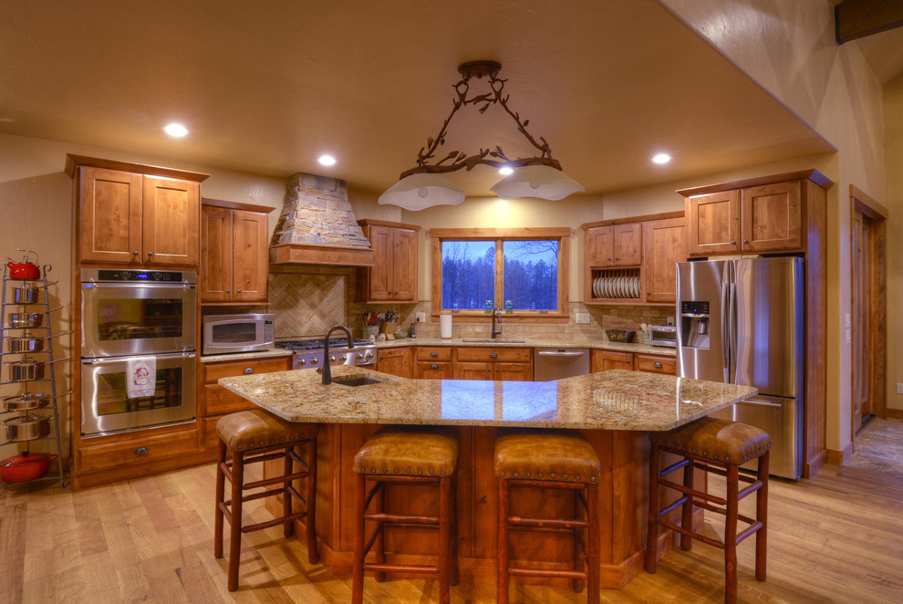 Inspiration for a transitional light wood floor open concept kitchen remodel in Denver with an undermount sink, raised-panel cabinets, medium tone wood cabinets, granite countertops, beige backsplash, stone tile backsplash, stainless steel appliances and an island