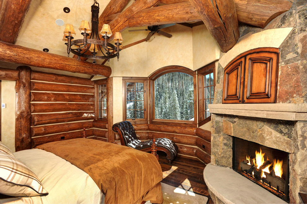 This is an example of a country guest bedroom in Denver with beige walls, dark hardwood floors, a standard fireplace, a stone fireplace surround and brown floor.
