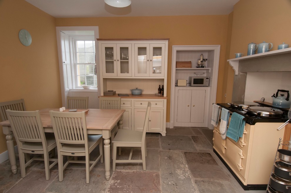 This is an example of a large traditional eat-in kitchen in Edinburgh with a farmhouse sink, white cabinets, coloured appliances, no island, glass-front cabinets and wood benchtops.