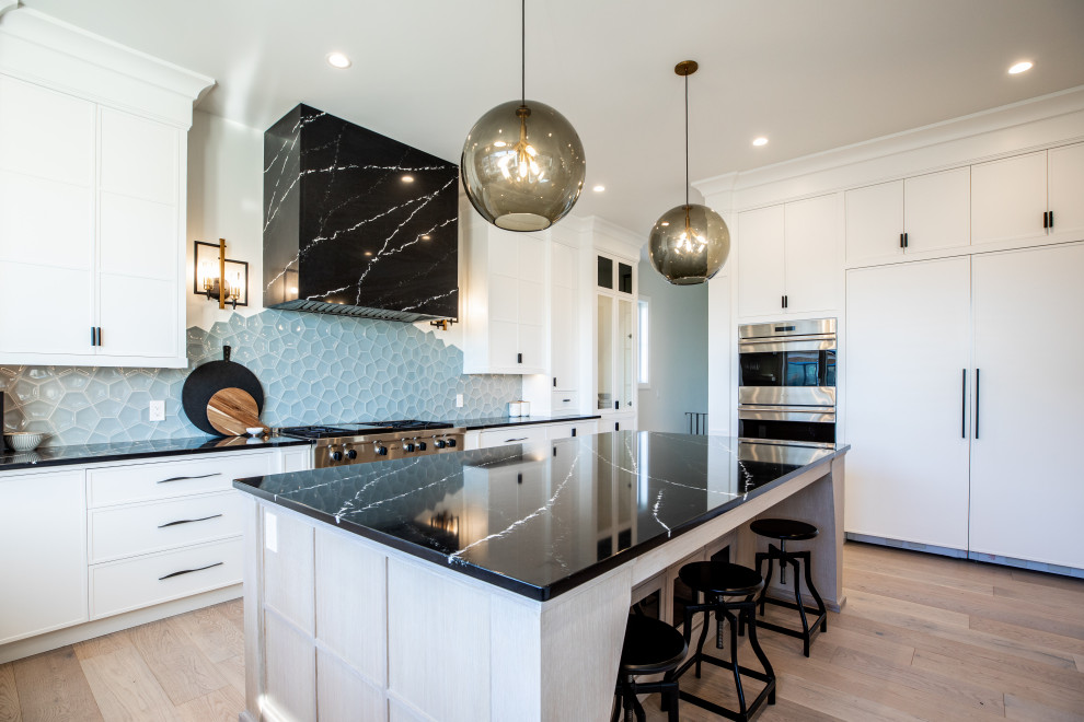 Inspiration for a large country u-shaped eat-in kitchen in Calgary with an undermount sink, recessed-panel cabinets, white cabinets, marble benchtops, blue splashback, glass tile splashback, stainless steel appliances, plywood floors, with island, brown floor and black benchtop.