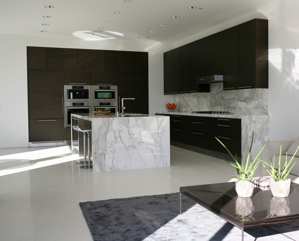 Mid-sized modern l-shaped open plan kitchen in Los Angeles with an undermount sink, flat-panel cabinets, dark wood cabinets, marble benchtops, white splashback, stone slab splashback, stainless steel appliances, concrete floors, with island, white floor and white benchtop.