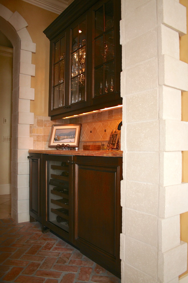 This is an example of a small traditional single-wall wet bar in Miami with raised-panel cabinets, dark wood cabinets, beige splashback, stone tile splashback, brick floors and marble benchtops.