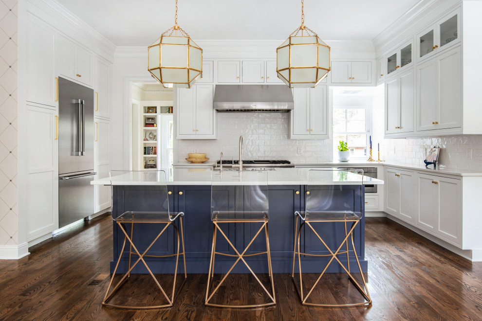 This is an example of a large traditional u-shaped kitchen/diner in Nashville with a belfast sink, beaded cabinets, white cabinets, engineered stone countertops, white splashback, ceramic splashback, stainless steel appliances, dark hardwood flooring, an island, brown floors and white worktops.
