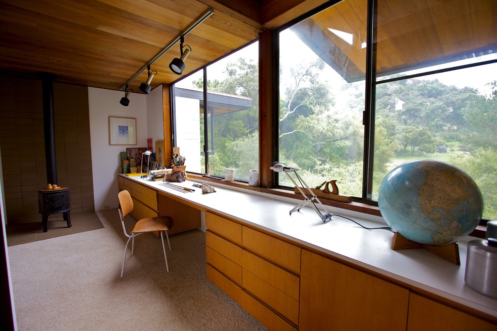 Photo of a mid-sized midcentury craft room in San Diego with white walls, a wood stove and a built-in desk.