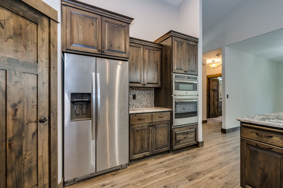 Open concept kitchen - large rustic u-shaped laminate floor and brown floor open concept kitchen idea with an undermount sink, raised-panel cabinets, medium tone wood cabinets, quartz countertops, beige backsplash, stainless steel appliances and an island