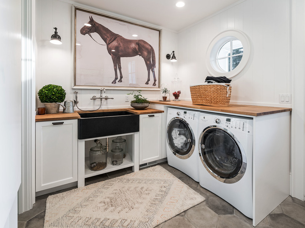 Design ideas for a country l-shaped laundry room in Portland with a farmhouse sink, recessed-panel cabinets, white cabinets, wood benchtops, a side-by-side washer and dryer, grey floor and brown benchtop.