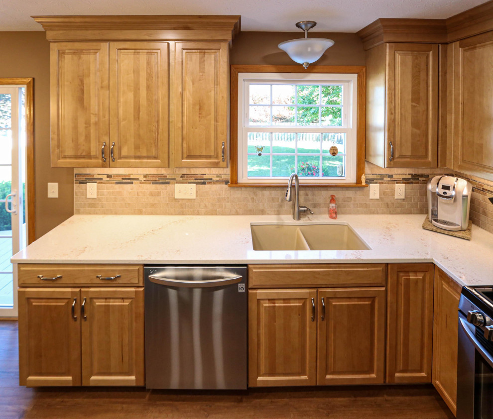 Photo of a mid-sized transitional l-shaped eat-in kitchen in Cleveland with an undermount sink, raised-panel cabinets, light wood cabinets, quartz benchtops, brown splashback, porcelain splashback, stainless steel appliances, vinyl floors, with island and brown floor.