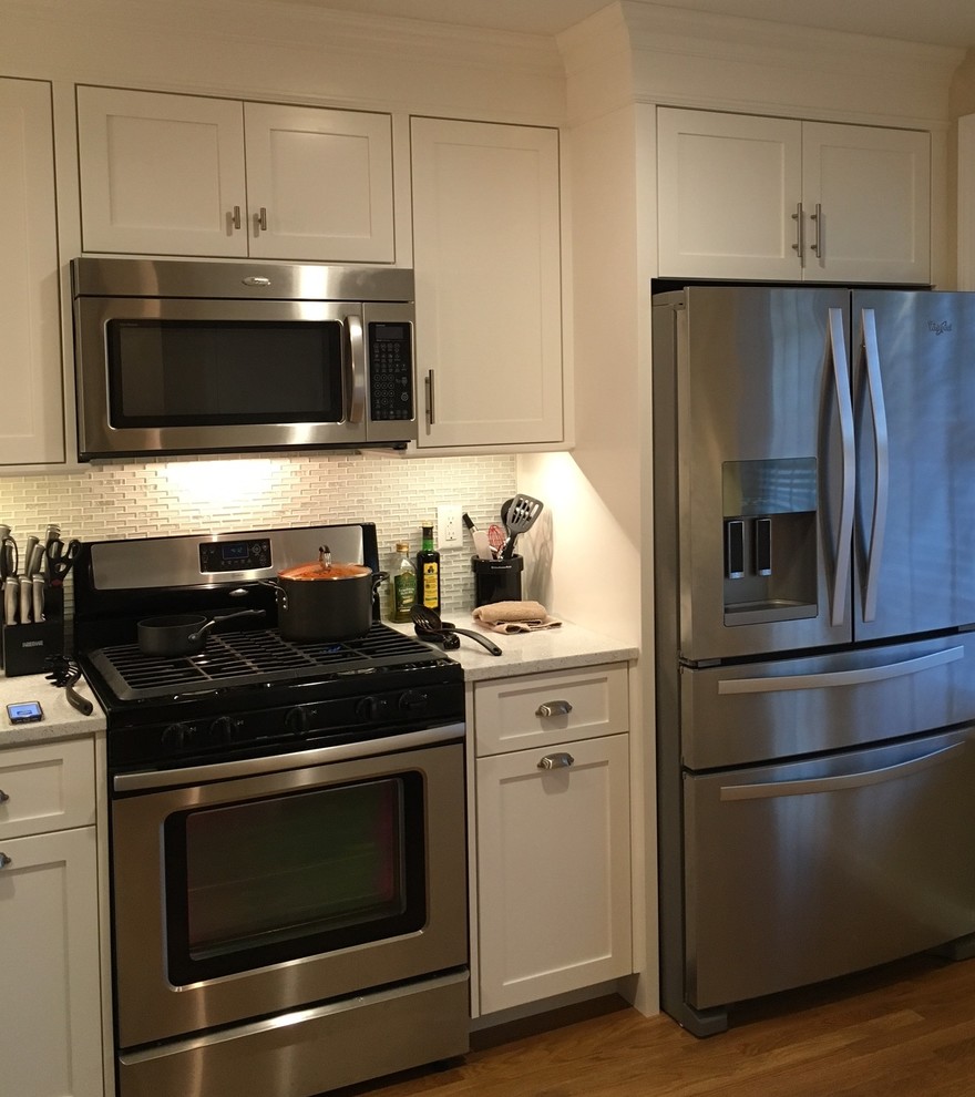 Mid-sized transitional light wood floor eat-in kitchen photo in Boston with recessed-panel cabinets, white cabinets, quartz countertops, multicolored backsplash, glass tile backsplash and stainless steel appliances