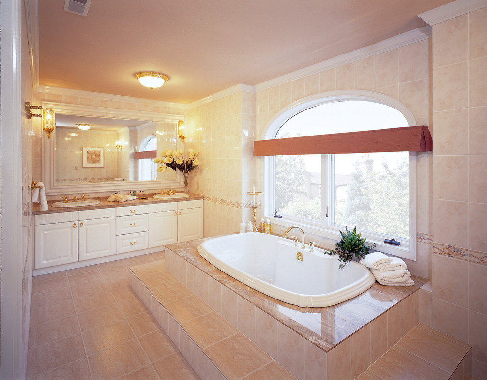 Inspiration for a traditional bathroom in Other with raised-panel cabinets, white cabinets, a corner tub, beige walls, marble floors and beige floor.