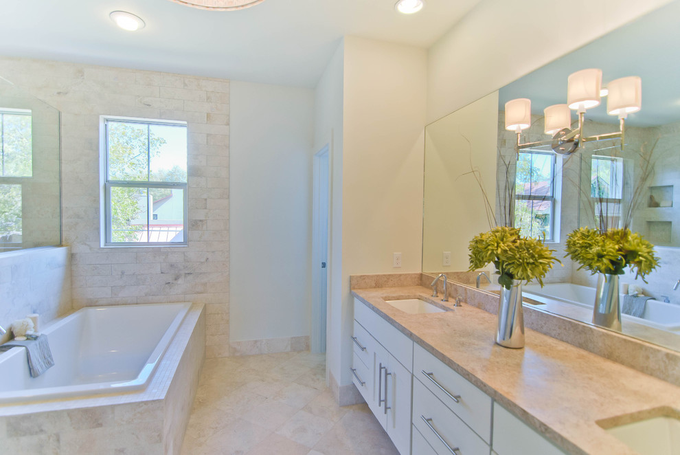 Photo of a contemporary bathroom in Austin with an undermount sink, flat-panel cabinets, white cabinets, a drop-in tub, beige tile and travertine.