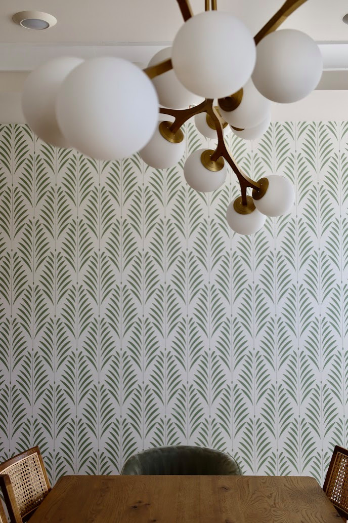 This modern dining room features a stunning geometric wallpaper in muted green, adding depth and texture to the space while reflecting nature-inspired design. A set of vintage-style cane dining chairs