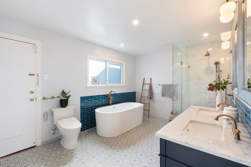 На фото: главная ванная комната среднего размера в стиле неоклассика (современная классика) с фасадами островного типа, синими фасадами, накладной ванной, угловым душем, биде, синей плиткой, керамической плиткой, белыми стенами, полом из мозаичной плитки, врезной раковиной, мраморной столешницей, серым полом, душем с распашными дверями, белой столешницей, тумбой под две раковины, встроенной тумбой и кессонным потолком