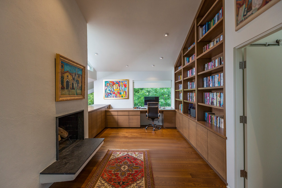 Photo of a mid-sized modern home office in Cincinnati with a library, white walls, medium hardwood floors, a stone fireplace surround, a built-in desk, brown floor and a standard fireplace.