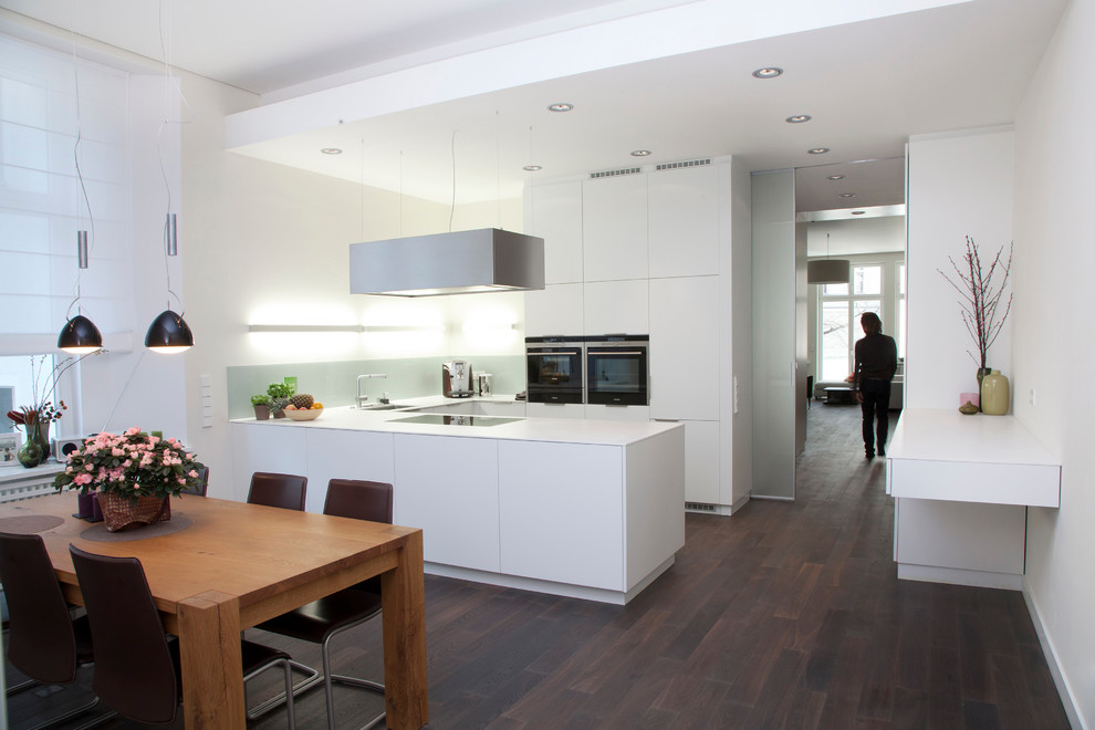 Large contemporary u-shaped open plan kitchen in Berlin with a drop-in sink, flat-panel cabinets, white cabinets, white splashback, stainless steel appliances, dark hardwood floors and a peninsula.