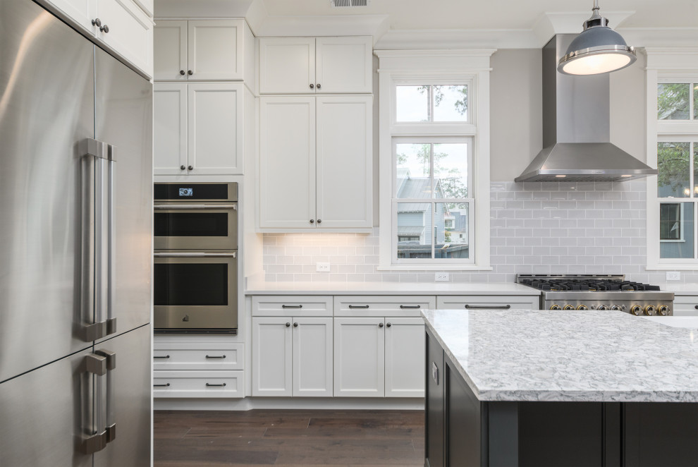 Inspiration for a transitional brown floor kitchen remodel with a farmhouse sink, gray backsplash, subway tile backsplash, stainless steel appliances, an island and white countertops