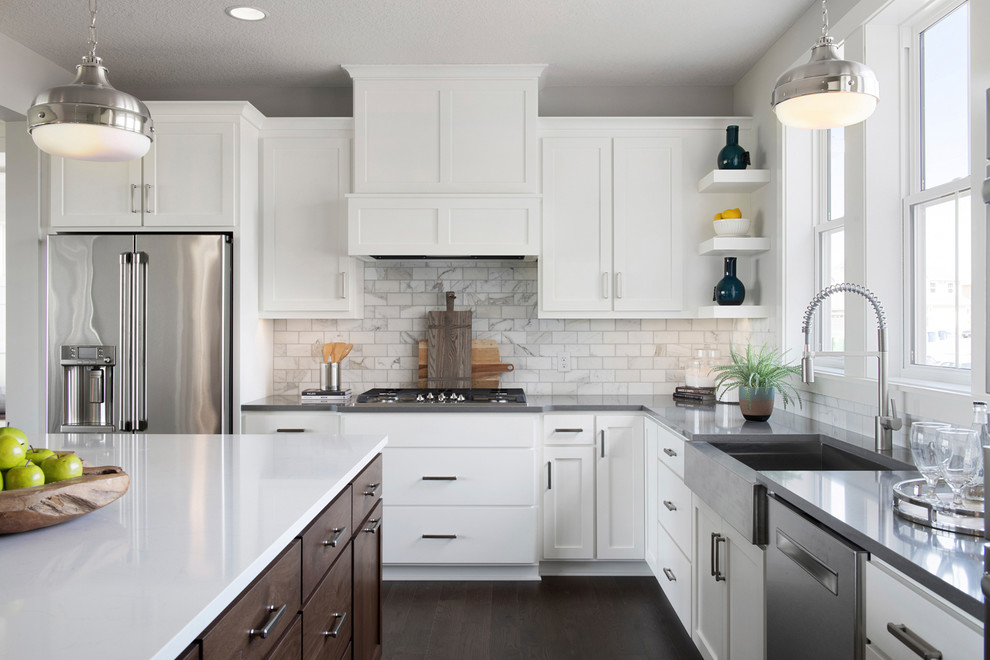 Expansive transitional l-shaped open plan kitchen in Minneapolis with a farmhouse sink, shaker cabinets, white cabinets, granite benchtops, grey splashback, subway tile splashback, stainless steel appliances, medium hardwood floors, with island and white benchtop.