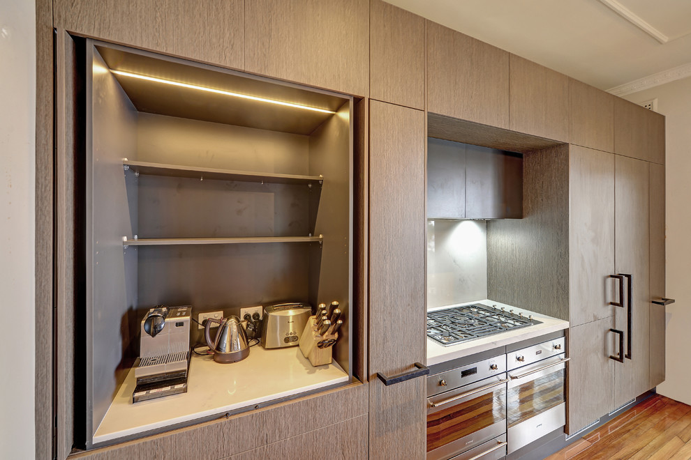 Mid-sized contemporary galley eat-in kitchen in Sydney with an undermount sink, flat-panel cabinets, grey cabinets, quartz benchtops, white splashback, stone slab splashback, stainless steel appliances, medium hardwood floors, with island, brown floor and white benchtop.