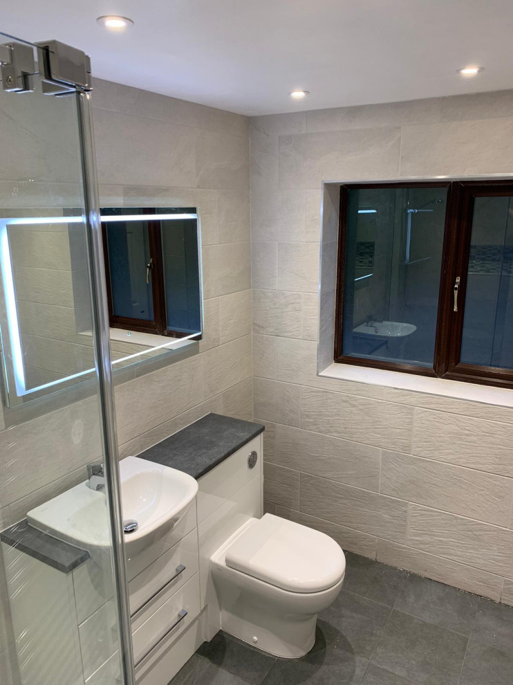 Photo of a medium sized modern grey and white ensuite bathroom in West Midlands with flat-panel cabinets, white cabinets, a built-in shower, a one-piece toilet, grey tiles, ceramic tiles, grey walls, porcelain flooring, a submerged sink, solid surface worktops, grey floors, an open shower, grey worktops, a feature wall, a single sink, a built in vanity unit and brick walls.