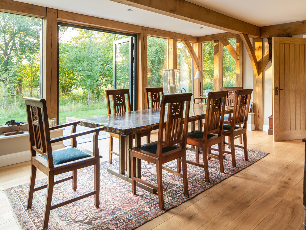 Country dining room in Surrey with white walls, medium hardwood flooring and exposed beams.