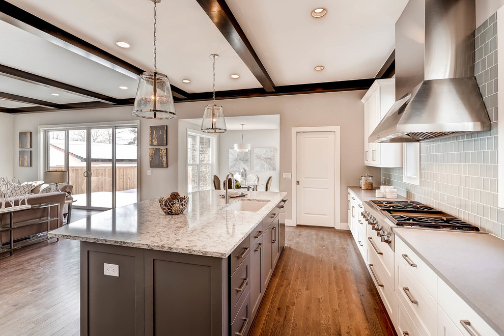 Inspiration for a large transitional l-shaped medium tone wood floor open concept kitchen remodel in Denver with an undermount sink, shaker cabinets, white cabinets, granite countertops, gray backsplash, glass tile backsplash, stainless steel appliances and an island