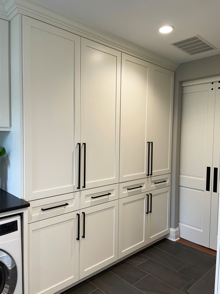 Design ideas for an expansive transitional laundry room in Milwaukee with a drop-in sink, shaker cabinets, white cabinets, granite benchtops, white splashback, subway tile splashback, grey walls, porcelain floors, a side-by-side washer and dryer, black floor and black benchtop.