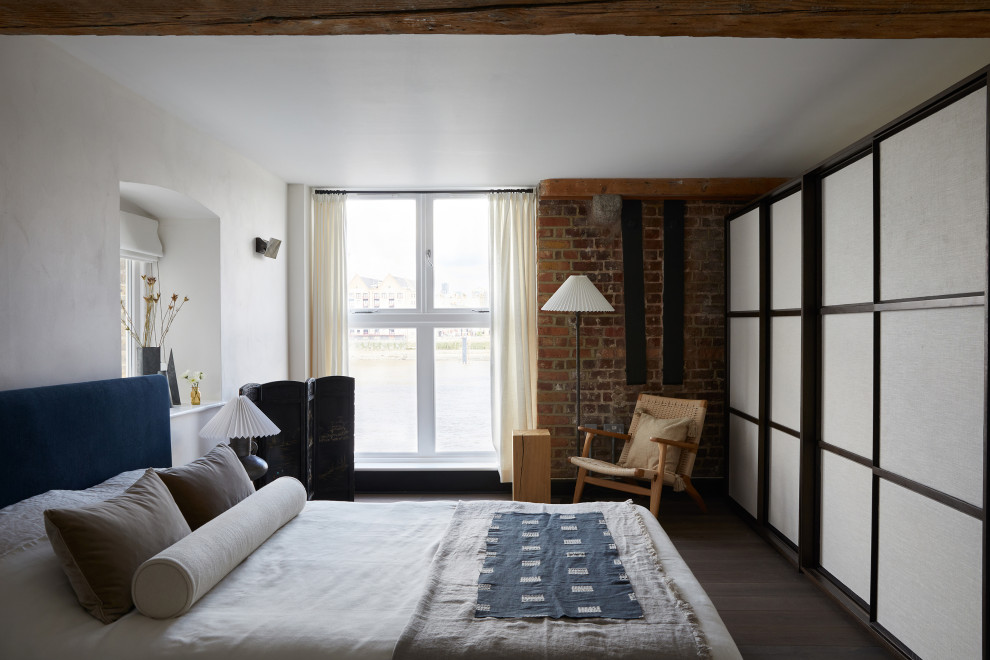 Diseño de dormitorio industrial con paredes blancas, suelo de madera oscura, suelo marrón y ladrillo