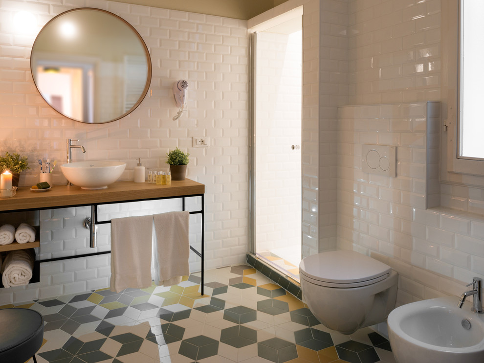 Photo of a small scandinavian 3/4 bathroom in Florence with open cabinets, medium wood cabinets, an alcove shower, a bidet, white tile, subway tile, white walls, cement tiles, a vessel sink, wood benchtops, multi-coloured floor and a hinged shower door.