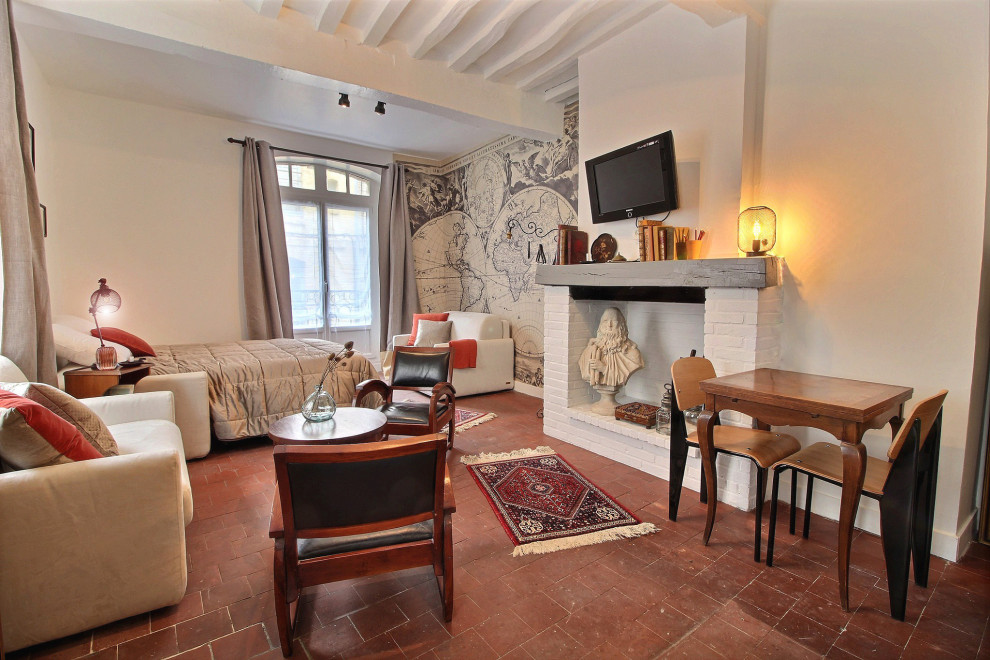 Kleines, Abgetrenntes Wohnzimmer ohne Kamin mit weißer Wandfarbe, Terrakottaboden, Kaminumrandung aus Holz, TV-Wand, rotem Boden, freigelegten Dachbalken und Tapetenwänden in Korsika