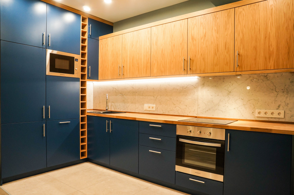 This is an example of a mid-sized l-shaped open plan kitchen in Moscow with an undermount sink, flat-panel cabinets, blue cabinets, wood benchtops, white splashback, porcelain splashback, stainless steel appliances, porcelain floors, with island, beige floor and beige benchtop.