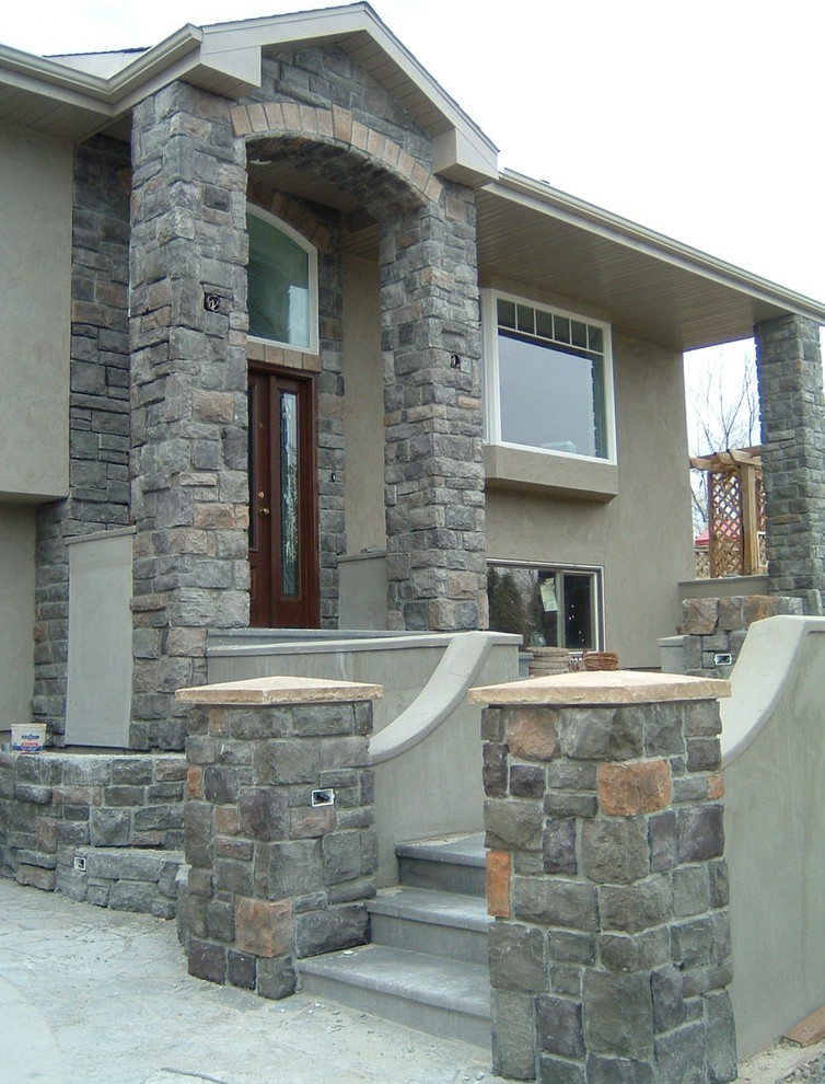 Photo of a large traditional two-storey stucco grey house exterior in Other with a clipped gable roof.