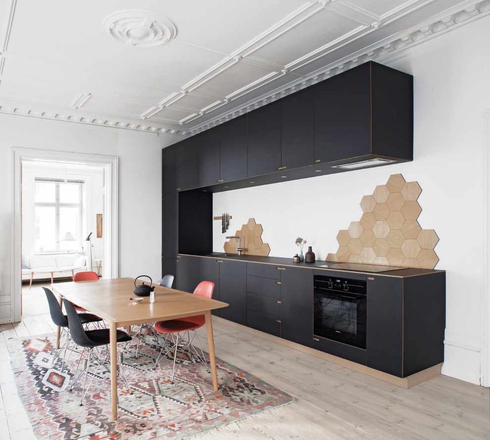 This is an example of a large scandinavian single-wall eat-in kitchen in Copenhagen with flat-panel cabinets, black cabinets, beige splashback, black appliances, light hardwood floors, no island, a drop-in sink and wood benchtops.