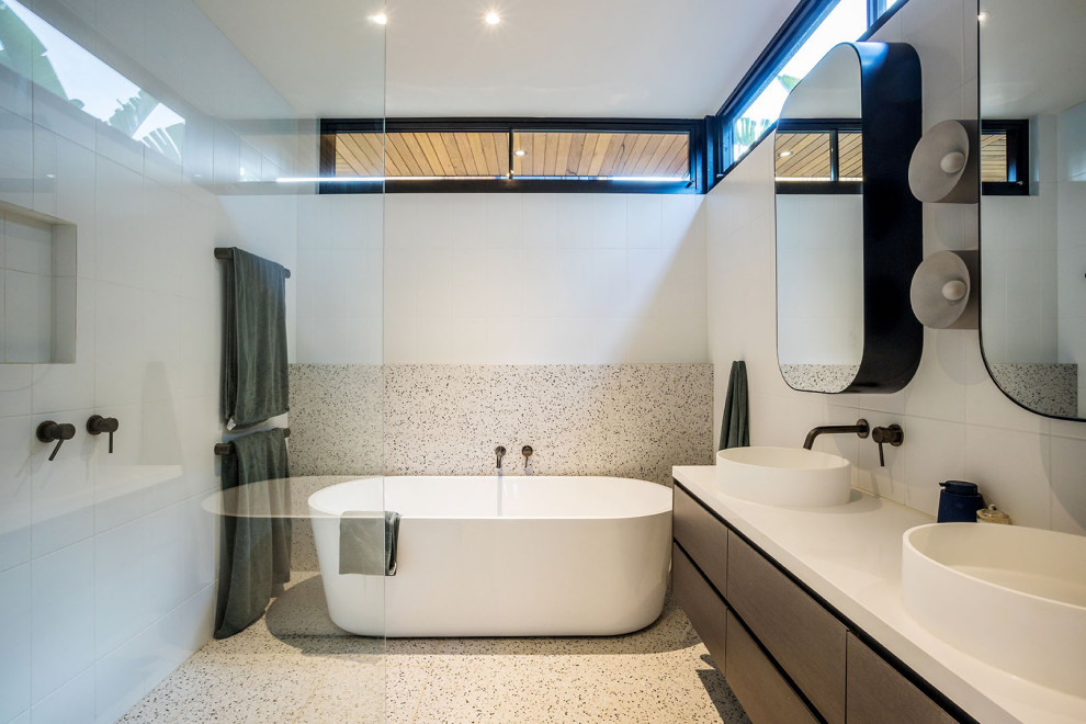 This is an example of a mid-sized contemporary master bathroom in Melbourne with a freestanding tub, white tile, terrazzo floors, an open shower, a double vanity, flat-panel cabinets, dark wood cabinets, a curbless shower, white walls, a vessel sink, multi-coloured floor, white benchtops and a floating vanity.